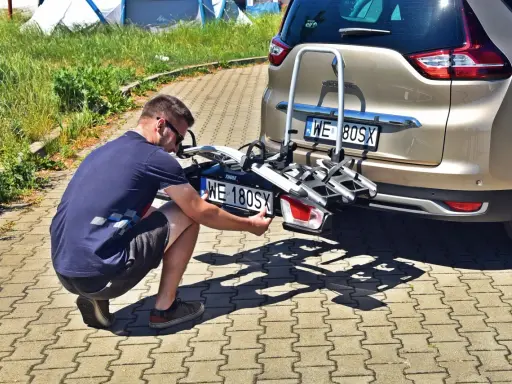 Mężczyzna montuje tablicę rejestracyjną na bagażnik rowerowy zamontowany z tyłu samochodu.