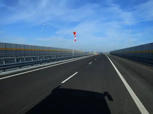 Pusta jezdnia nowej drogi z barierami dźwiękochłonnymi i wiatrowskazem.