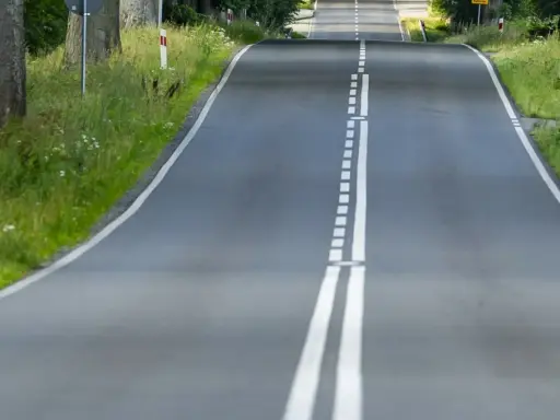 Droga wijąca się wśród zieleni, z podwójną białą **linią ciągłą** pośrodku.