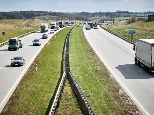 Ciężarówki na autostradzie pędzą z dużą prędkością, pokonując kolejne kilometry. W tle widać inne pojazdy i krajobraz.