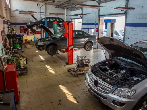Warsztat samochodowy z kilkoma autami na podnośnikach. Widać m.in. ciemny sedan, który wygląda jak p1351 peugeot, oraz srebrny SUV z otwartą maską.