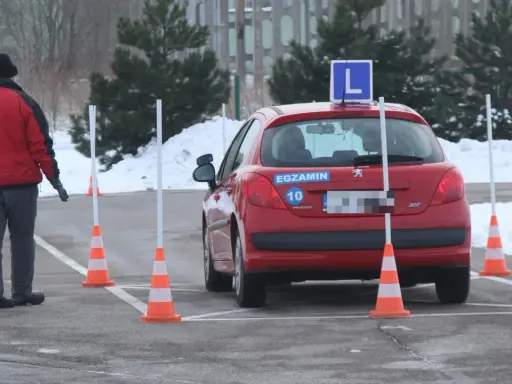 Czerwony samochód z literą "L" na dachu i naklejką "EGZAMIN" na tylnej klapie, otoczony pachołkami na placu manewrowym. To miejsce, gdzie bije rekord zdawania prawa jazdy.