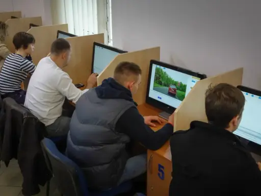 Ludzie siedzą przy komputerach, rozwiązując testy. Tak sprawdzisz, jak zdałeś egzamin teoretyczny na prawo jazdy.