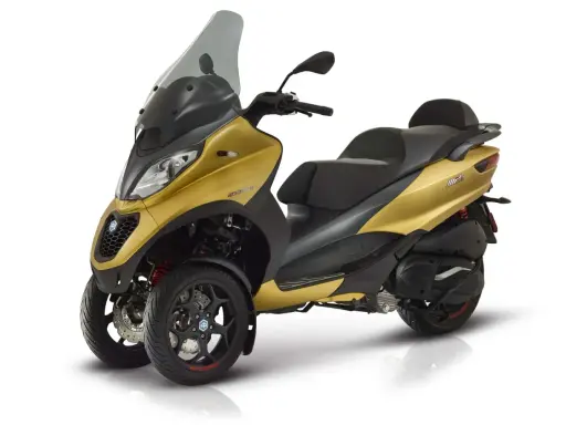 Złoty Piaggio MP3 500, trójkołowy skuter, gotowy do osiągnięcia swojej maksymalnej prędkości.