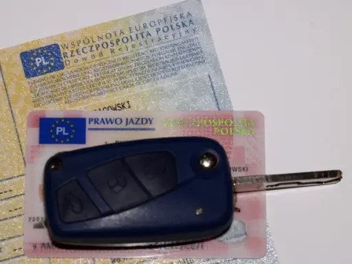 Kluczyk samochodowy leży na dowodzie rejestracyjnym i prawie jazdy. To komplet dokumentów do prowadzenia pojazdu.