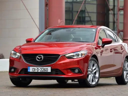 Czerwona Mazda 6, reprezentantka klasy D samochodów, prezentuje się elegancko na tle nowoczesnej architektury.