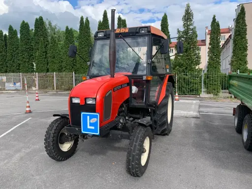 Czerwony traktor Zetor z tabliczką "L" na masce, gotowy do egzaminu na prawo jazdy na traktor.