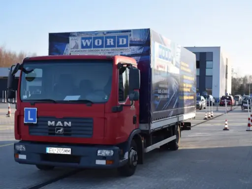 Czerwona ciężarówka MAN z literą "L" na masce i logo WORD. Na naczepie widnieje napis "WOJEWÓDZKI OŚRODEK RUCHU DROGOWEGO". To miejsce, gdzie składa się wniosek PKZ.