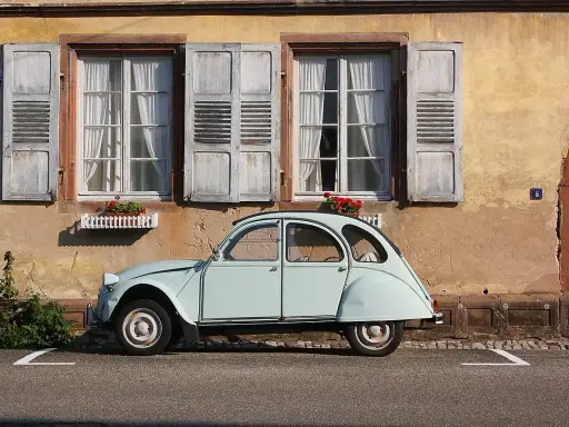 Jasnoniebieski, zabytkowy Citroen 2CV, jeden z tych klasycznych, francuskich modele stare, stoi przed kamiennym domem z drewnianymi okiennicami.