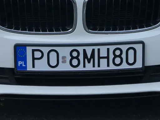 Biała tablica rejestracyjna z kodem PO 8MH80, z niebieskim paskiem UE i literami PL.