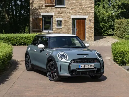 Nowoczesny Mini Cooper w kolorze miętowym stoi przed kamiennym domem. Zastanawiasz się, ile pali ten model?