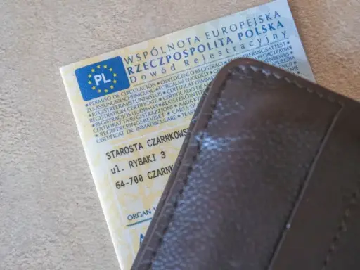 Dowód rejestracyjny pojazdu i brązowy portfel. Nieodebranie dokumentu może skutkować karą za nieodebranie dowodu rejestracyjnego.