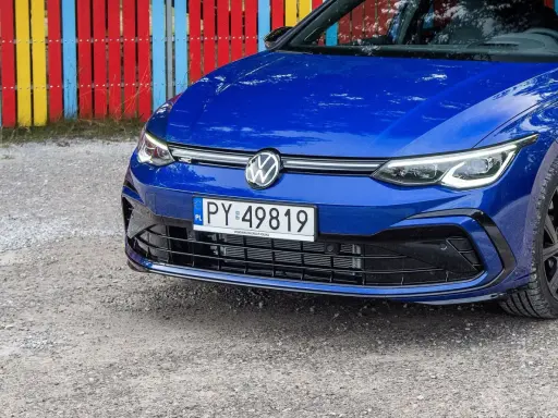 Niebieski Volkswagen Golf R z tablicą rejestracyjną PY 49819, zaparkowany przy kolorowym płocie.
