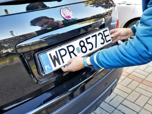 Mężczyzna montuje tablicę rejestracyjną. Pamiętaj o ważności dowodu rejestracyjnego, aby uniknąć problemów.