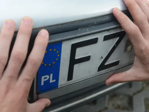 Dłonie trzymają tablicę rejestracyjną z oznaczeniem FZ.