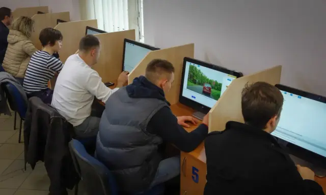 Ludzie siedzą przy komputerach, rozwiązując testy. Tak sprawdzisz, jak zdałeś egzamin teoretyczny na prawo jazdy.