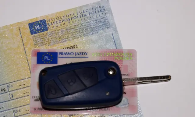 Kluczyk samochodowy leży na dowodzie rejestracyjnym i prawie jazdy. To komplet dokumentów do prowadzenia pojazdu.
