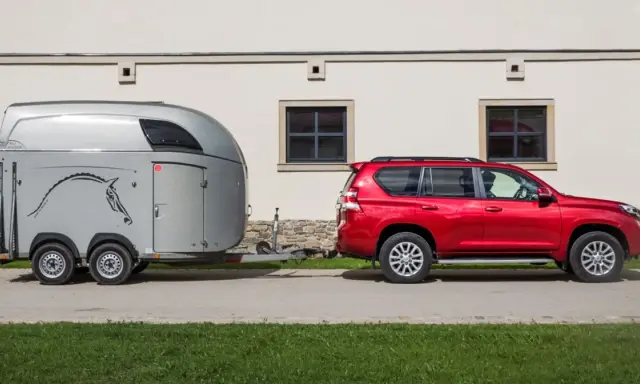 Czerwony SUV holuje przyczepę kempingową z koniem. Jaka kategoria na auto? SUV z przyczepą do przewozu zwierząt.