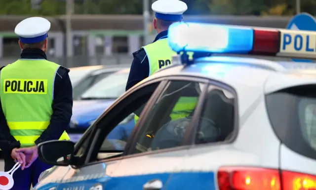 Policjanci w kamizelkach odblaskowych stoją przy radiowozie. Zastanawiasz się, ile można jechać poza terenem zabudowanym?