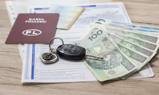 Karta pojazdu, kluczyki i polskie banknoty 100 zł leżą na dokumentach.