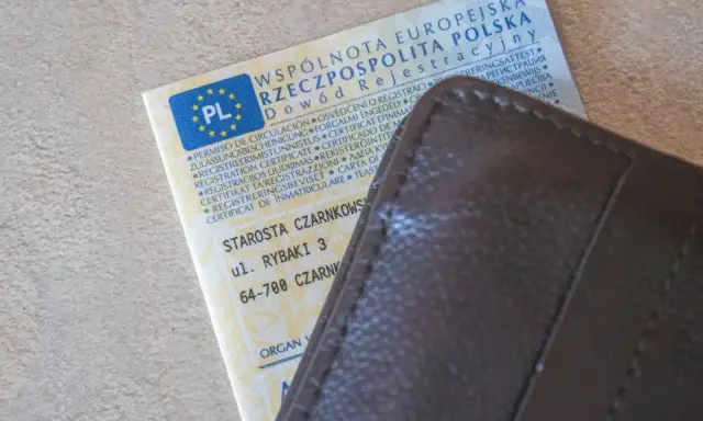 Dowód rejestracyjny pojazdu i brązowy portfel. Nieodebranie dokumentu może skutkować karą za nieodebranie dowodu rejestracyjnego.