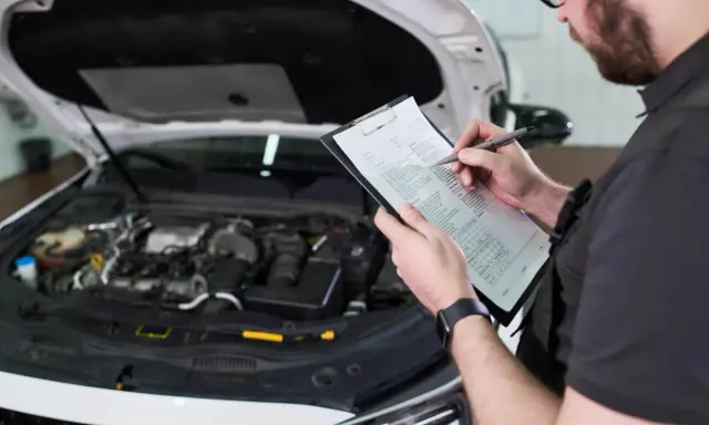 Mechanik sprawdza listę kontrolną przed przeglądem samochodu, zastanawiając się, ile kosztuje przegląd.