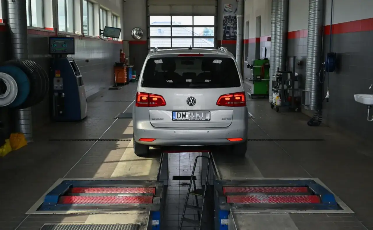 Srebrny Volkswagen Touran na podnośniku w warsztacie. Zastanawiasz się, ile kosztuje przegląd?
