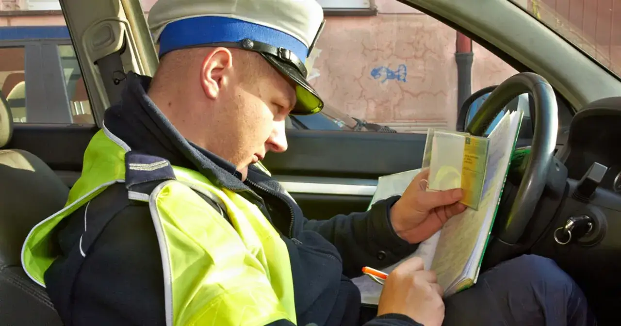 Policjant w kamizelce odblaskowej sprawdza dokumenty, być może w związku z zatrzymaniem dowodu rejestracyjnego.