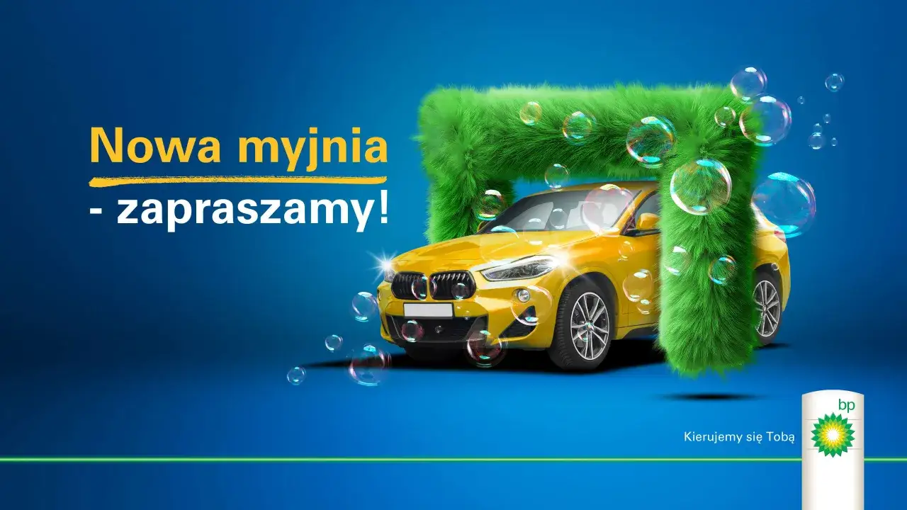 Nowa myjnia BP zaprasza! Żółty samochód wjeżdża w zieloną, puszystą bramę myjni, otoczony bańkami mydlanymi.