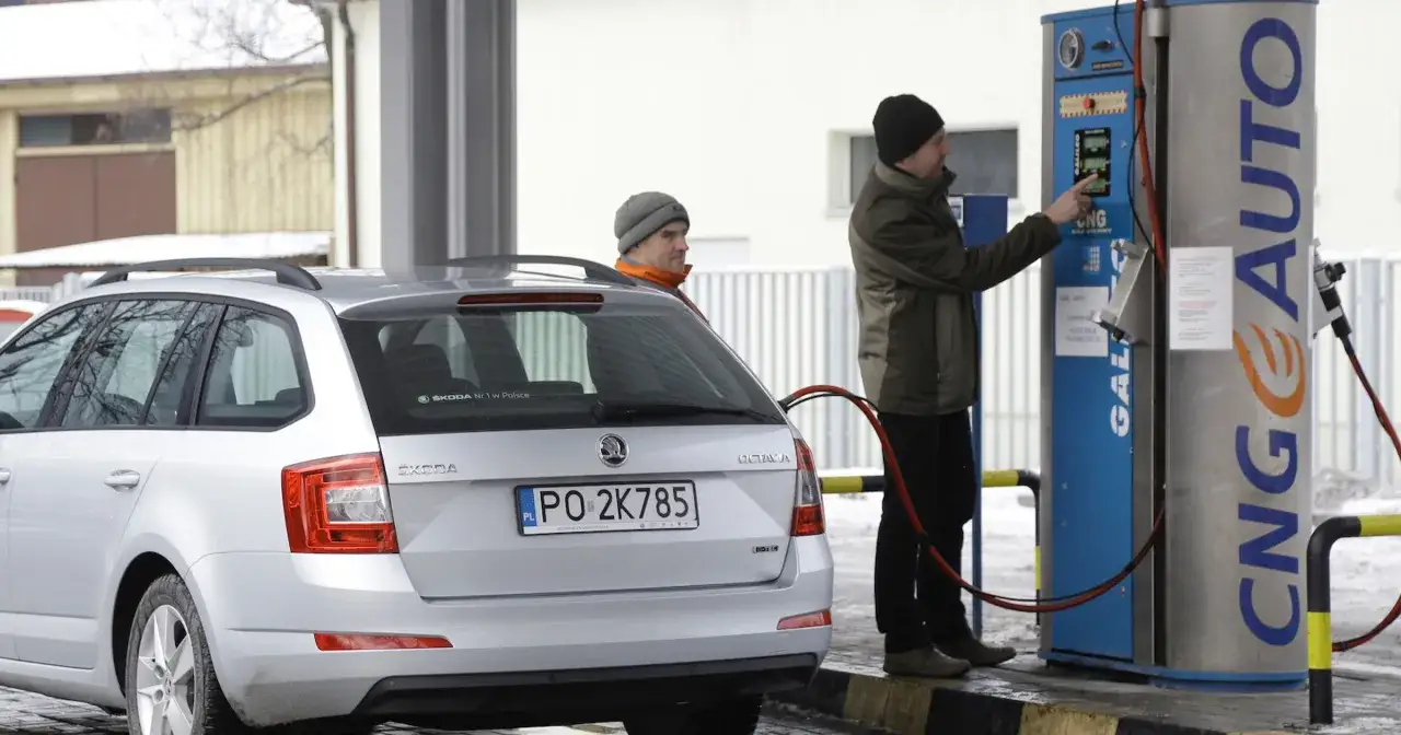 Mężczyzna tankuje gaz CNG do srebrnego kombi. Na dystrybutorze widnieje napis