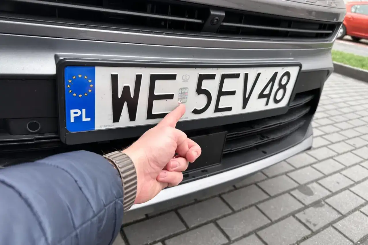 Dłoń wskazuje na hologram na tablicy rejestracyjnej. Ciekawe, ile się czeka na tablice rejestracyjne w Polsce.