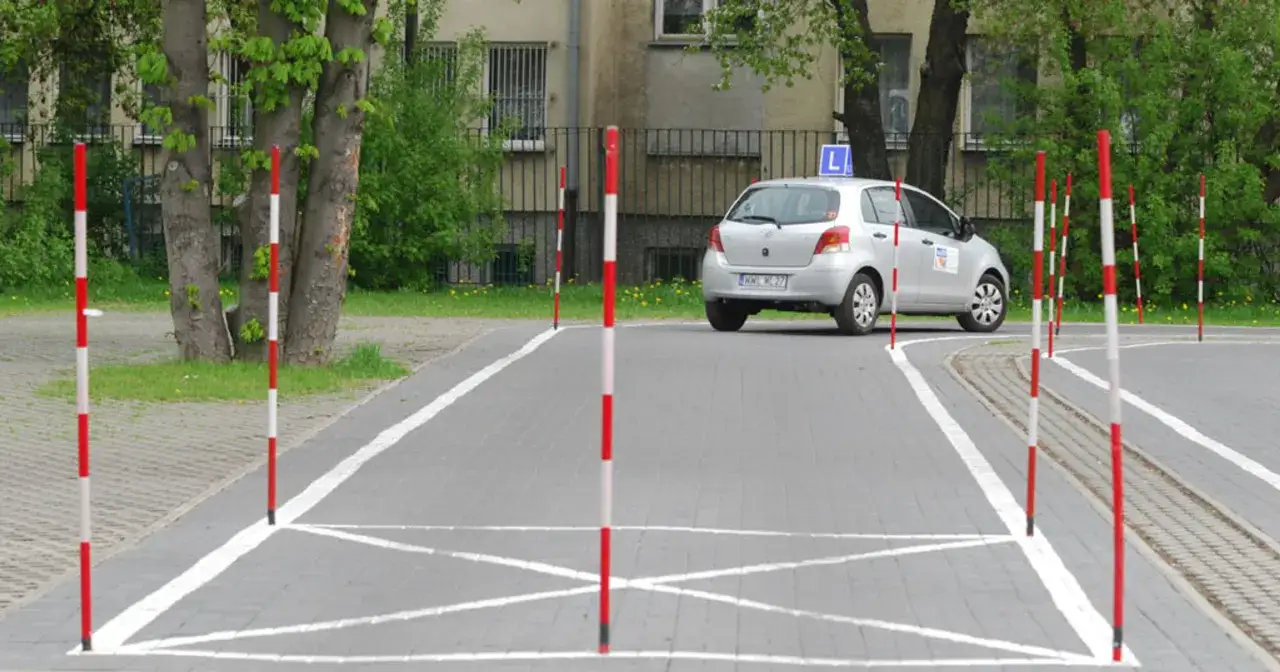 Plac manewrowy z tyczkami, na którym stoi srebrny samochód z literą 