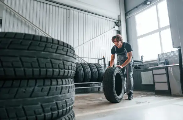 Mechanik w warsztacie przygotowuje opony zimowe przy 20 stopniach. Stosy opon czekają na wymianę.